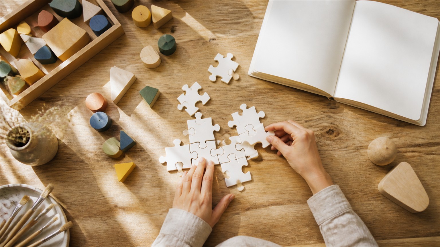Hands arranging blank jigsaw pieces and colored wooden shapes on a creative studio desk.