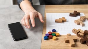 A hand moving from a face-down phone toward physical puzzle pieces and a blank grid.