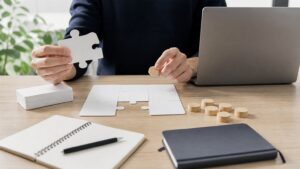 Hands reviewing blank puzzle cards, wooden tokens, and a closed notebook on a research desk.